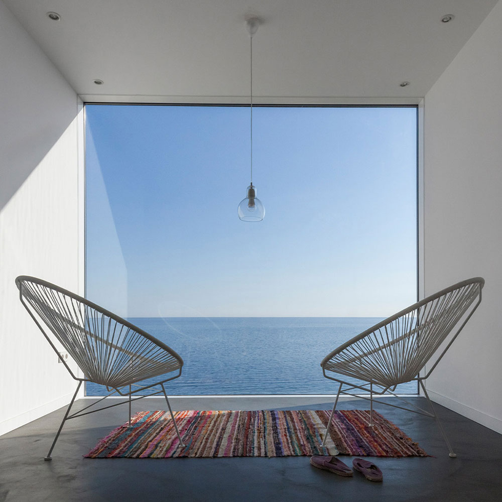 Два модерни стола и килим от Studio28a са обърнати към гледката към океана; висящо осветление допълва интериорен дизайн.