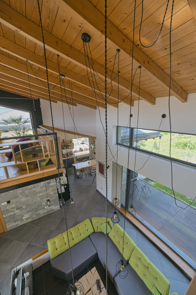 Модерна дневна от Интериорен дизайн Studio28a с открит дървен таван, висящи лампи и зелен секционен диван.