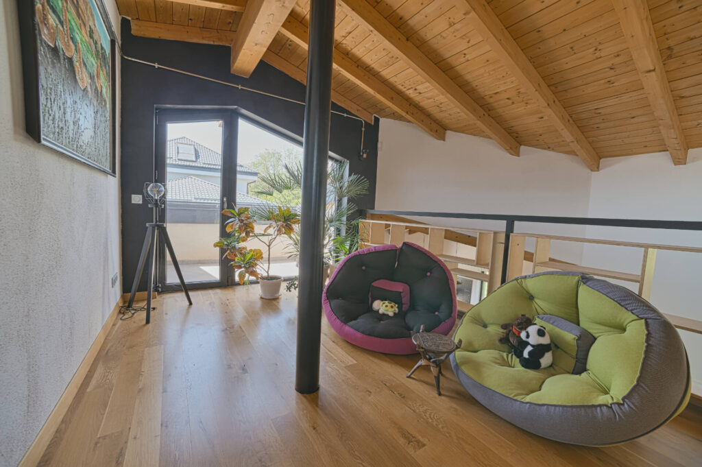Таванска стая от Интериорен дизайн Studio28a с дървен таван, плюшени играчки, растения и очарователно стенно изкуство.