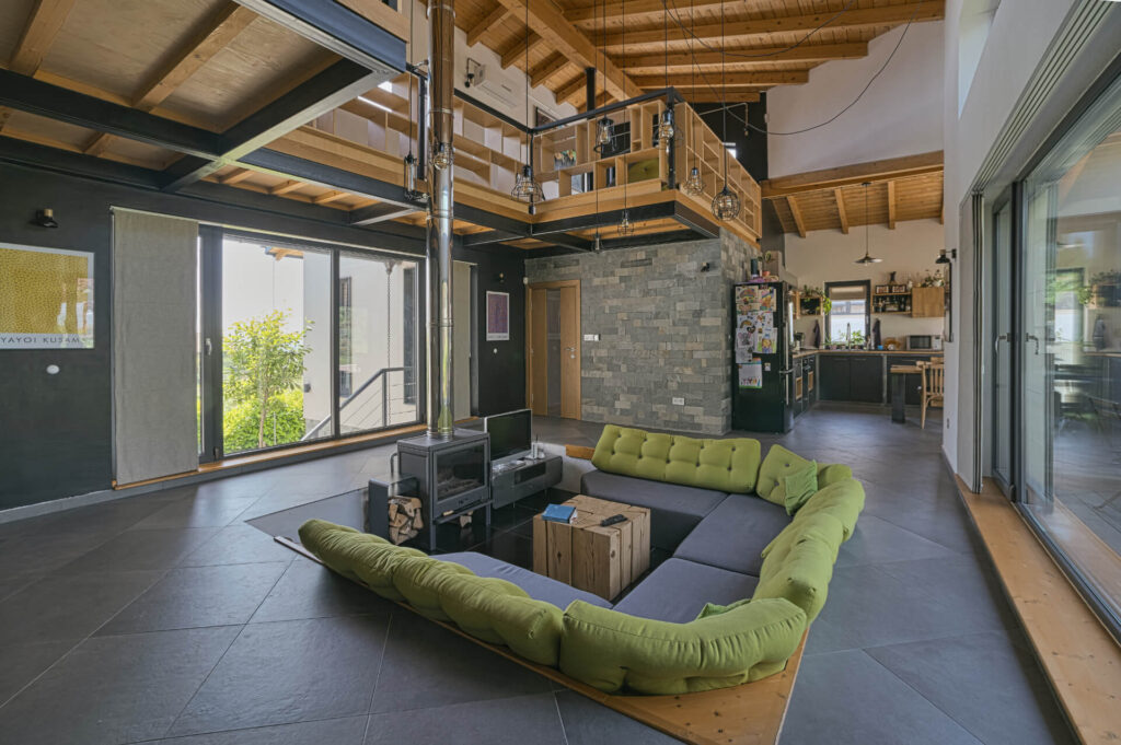 Модерна дневна с отворен план от Интериорен дизайн Studio28a с потънал зелен диван, печка на дърва, мецанин и големи прозорци.