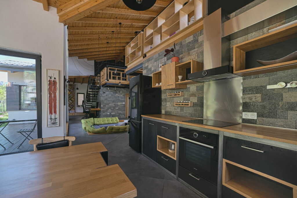 Модерна кухня с отворен план от Интериорен дизайн Studio28a, с дървени и каменни облицовки, таванско помещение и зелен диван на заден план.