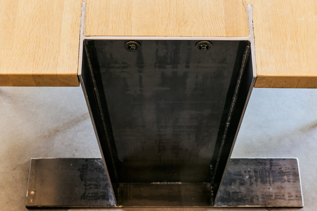 Близък план на метален крак на маса от Интериорен дизайн Studio28a, който поддържа дървен плот върху бетонен под.