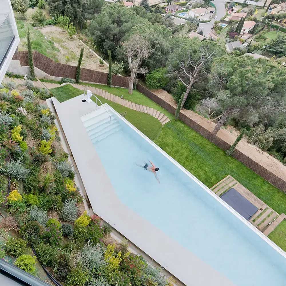 Човек плува сам в правоъгълен басейн до озеленена градина, проектиран от Интериорен дизайн Studio28a.