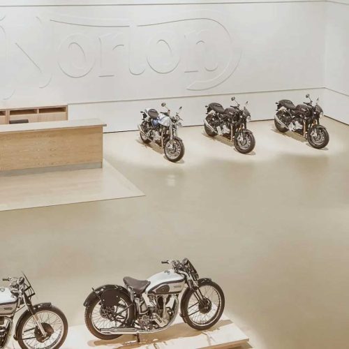 Пет мотоциклета са изложени в просторна галерия, проектирана от Интериорен дизайн Studio28a, с голямо лого на Norton отзад.