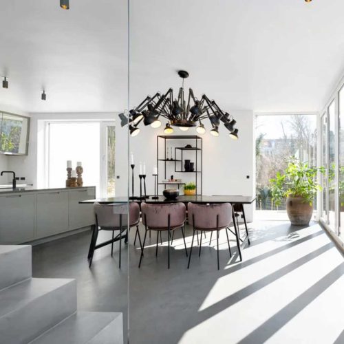 Модерна трапезария от Интериорен дизайн Studio28a с черна маса, розови столове, полилей и слънчеви прозорци.