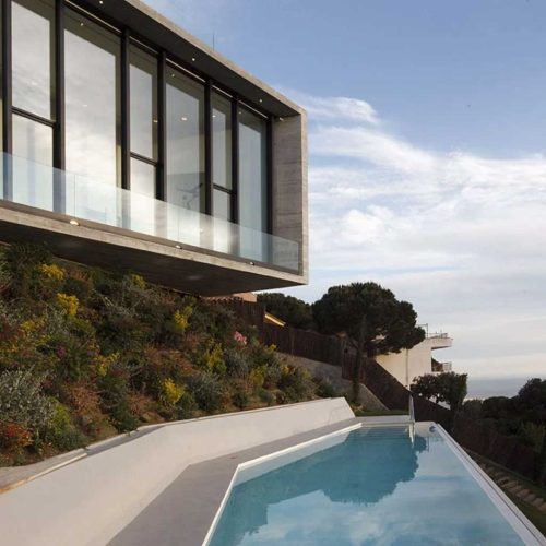 Модерна къща с прозорци от пода до тавана от Интериорен дизайн Studio28a с изглед към басейн и озеленен склон.