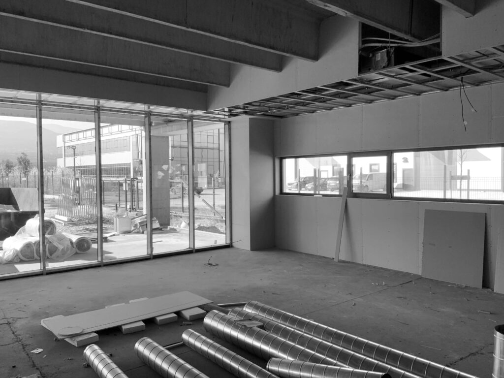 Незавършен търговски интериор от Интериорен дизайн Studio28a, с открити въздуховоди, отворен таван и големи прозорци.