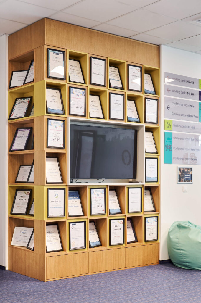 Дървена етажерка с телевизор и сертификати в рамка, проектирана от Интериорен дизайн Studio28a за офис.