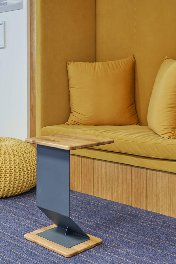 Малка дървена странична масичка с горчичножълта пейка и плетен пуф, създадена от Интериорен дизайн Studio28a.