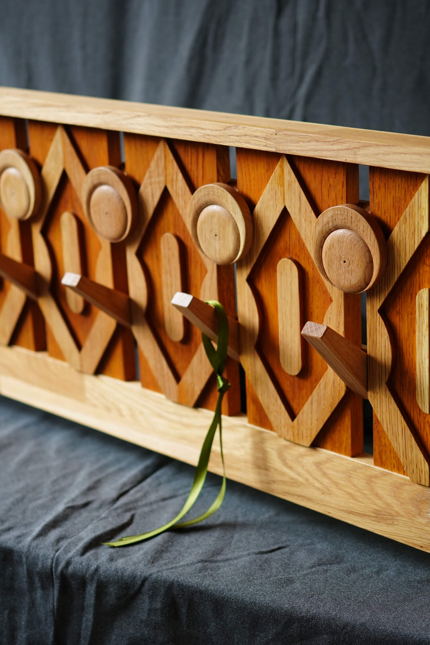 Дървена закачалка за дрехи с кръгли и ромбовидни мотиви от Интериорен дизайн Studio28a, с пет колчета и зелена панделка.