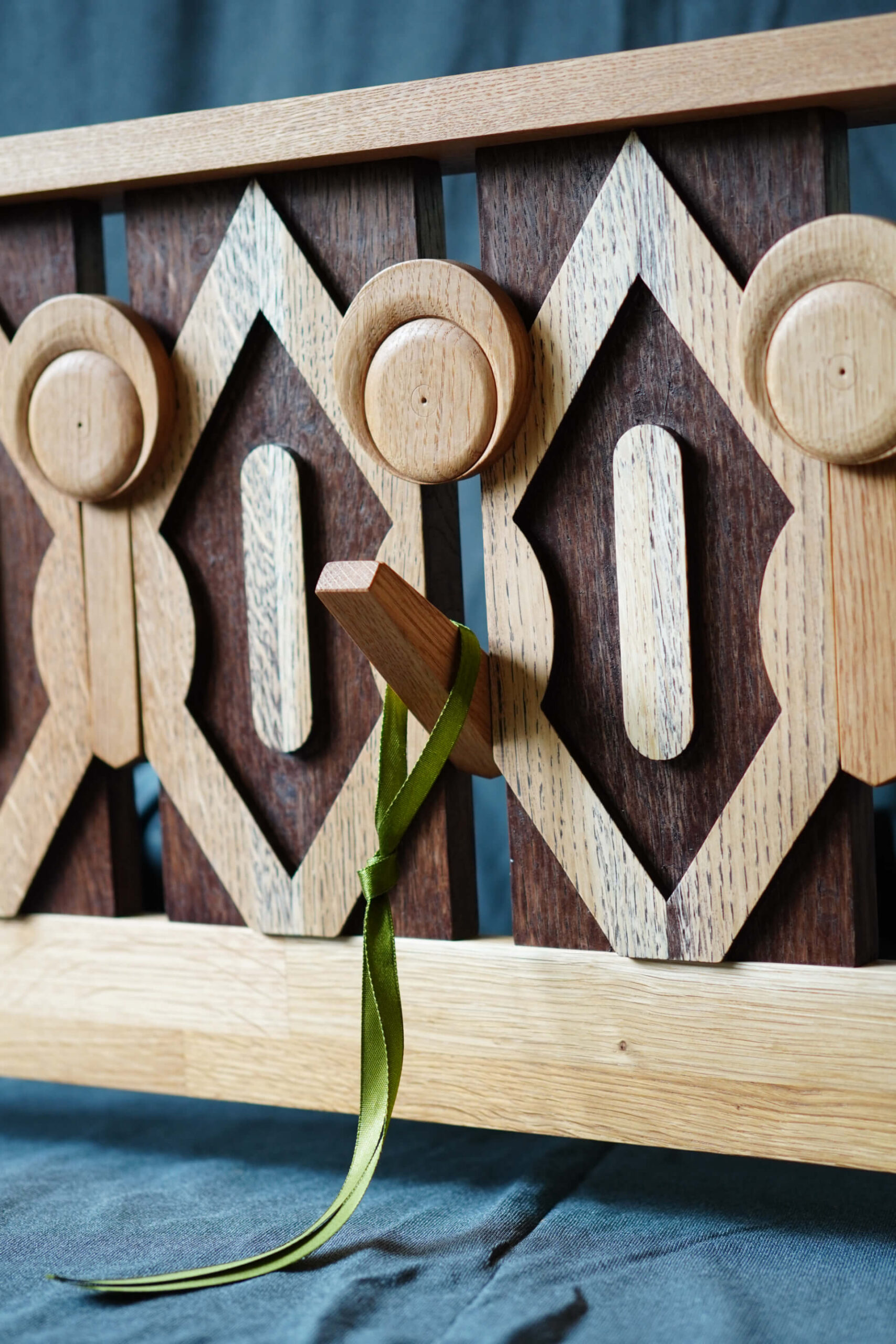 Близък план на дървено декоративно пано от Интериорен дизайн Studio28a, с геометрични шарки и зелена панделка на колче.