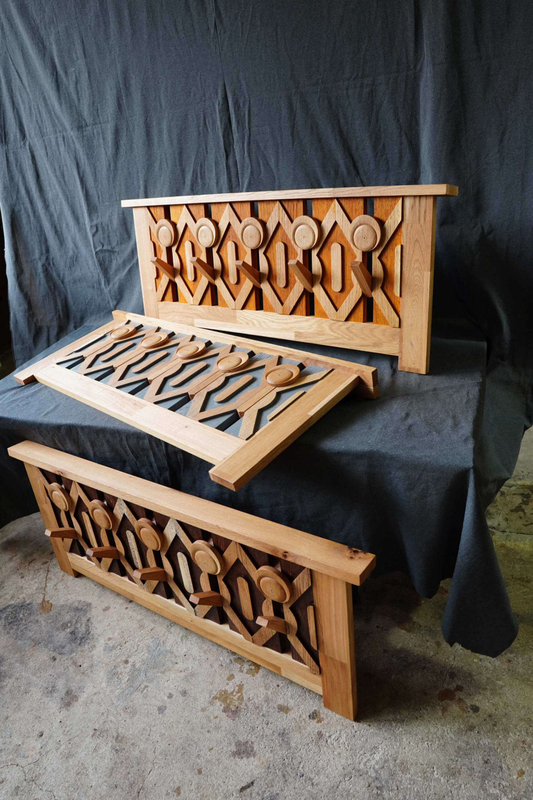 Три дървени панела с геометрични изрезки от Интериорен дизайн Studio28a, изложени върху тъмен плат и бетонен под.