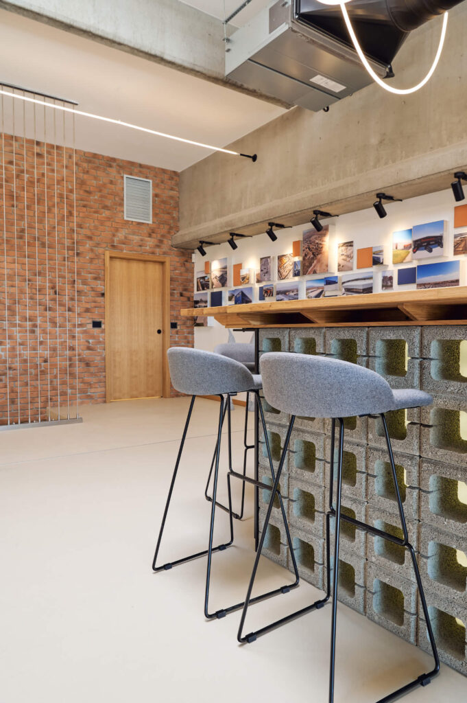 Модерен бар от Интериорен дизайн Studio28a със сиви табуретки, плот от бетонни блокове, тухлени стени и дисплеи за снимки над тях.