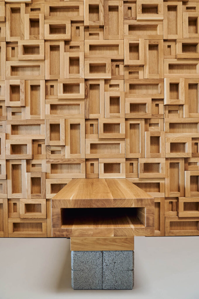 Дървена пейка с кух център се намира пред геометрична стена от Интериорен дизайн Studio28a.