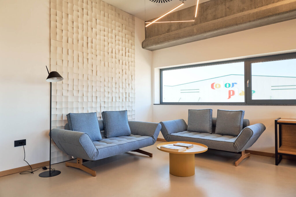 Модерна зона за отдих от Интериорен дизайн Studio28a със сини дивани, масичка за кафе, произведения на изкуството на стената и естествена светлина.