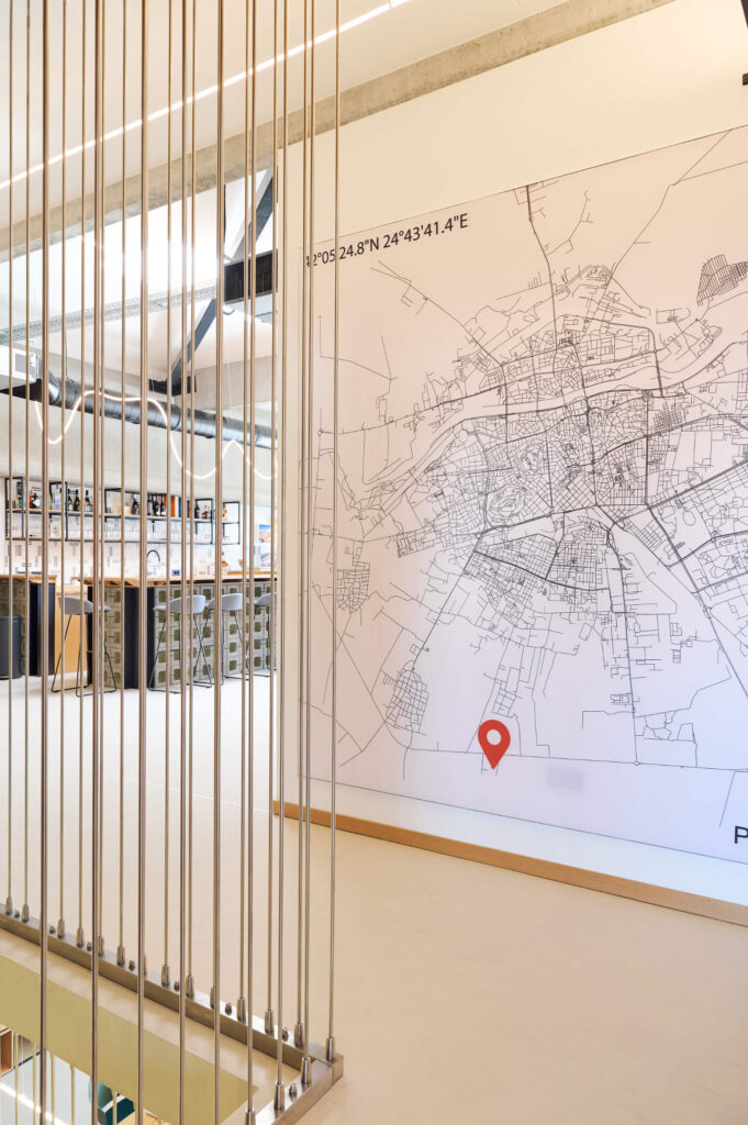 Голяма стенна карта с координати и червена карфица, акцентираща върху модерния интериорен дизайн Studio28a с рафтове и книги.