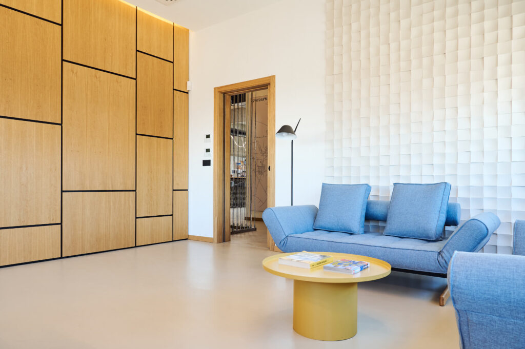 Модерна дневна от Интериорен дизайн Studio28a с дървена ламперия, 3D бяла стена, син диван и жълта масичка за кафе.