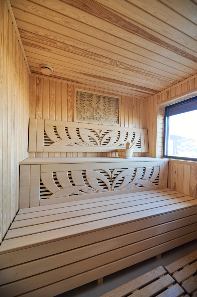 Облицована с дърво стая за сауна от Интериорен дизайн Studio28a с пейки, ведро и прозорец с изглед към градските сгради.