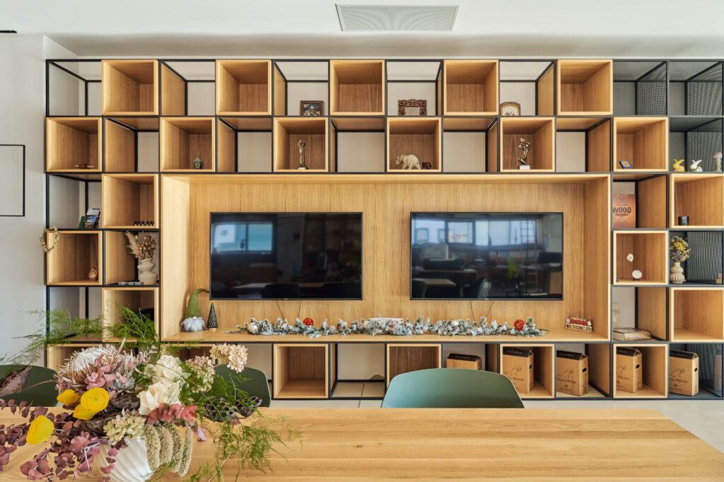 Модерен стенен модул от Интериорен дизайн Studio28a с отворени рафтове, два телевизора и декор зад дървена маса.