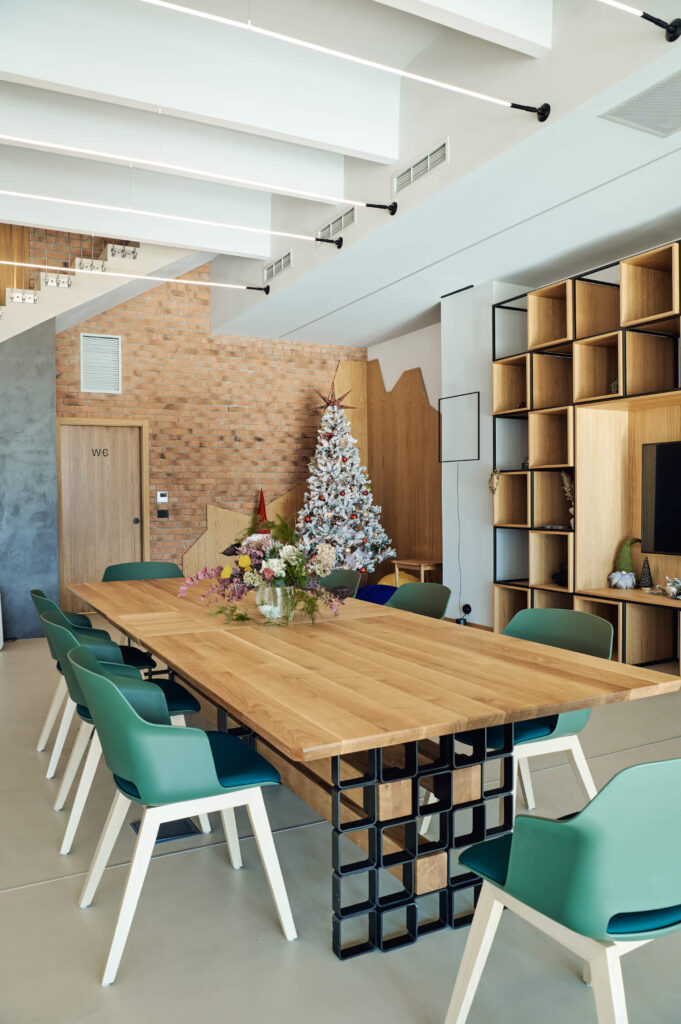 Модерна заседателна зала с дълга дървена маса, зелени столове и Интериорен дизайн Studio28a празнични елементи.