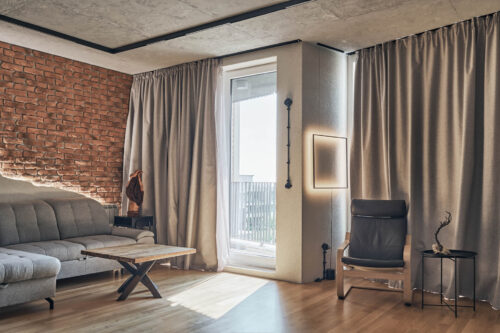 Модерна дневна от Интериорен дизайн Studio28a с тухлена стена, сив диван, фотьойл и голям прозорец.
