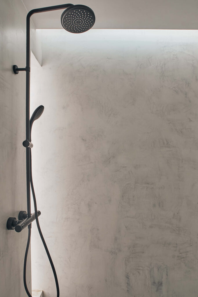 Минималистичен душ от Интериорен дизайн Studio28a с голяма кръгла душ-глава и ръчна пръскачка върху текстурирана сива стена.