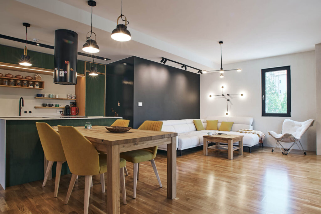 Модерна дневна с отворен план от Интериорен дизайн Studio28a с дървени подове, зелена кухня, жълти столове и бял диван.