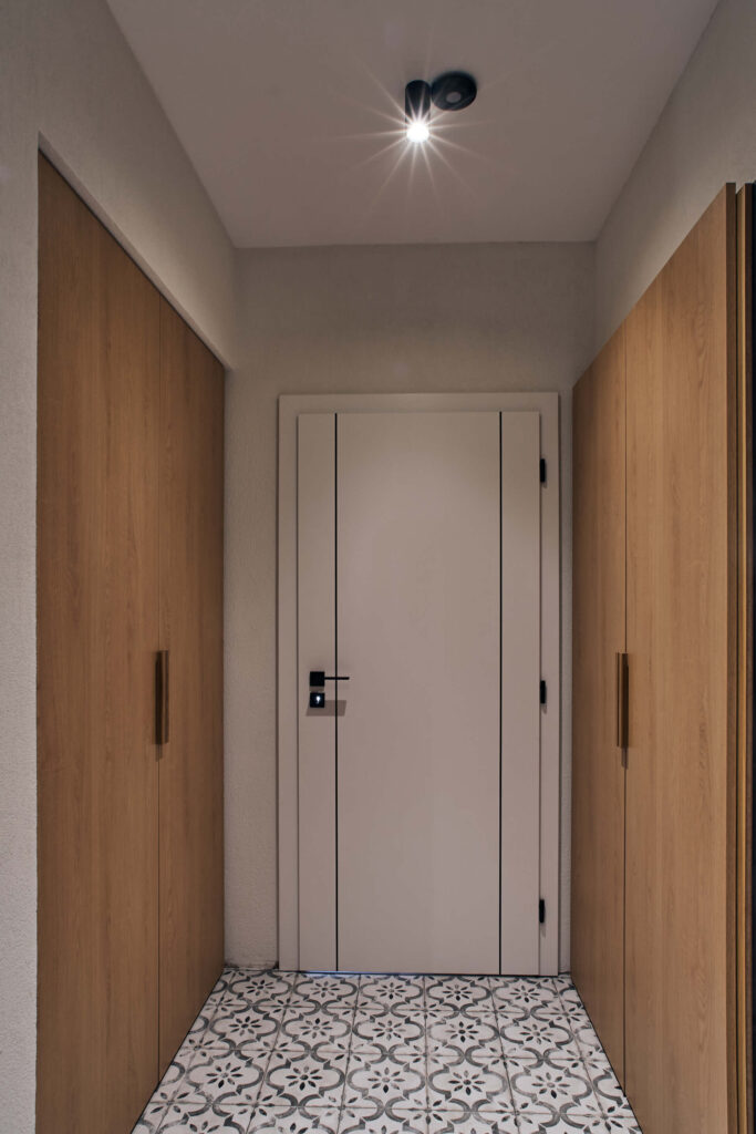 Коридор с шарени подови плочки, дървени врати на гардероба и обикновена бяла врата, проектиран от Интериорен дизайн Studio28a.
