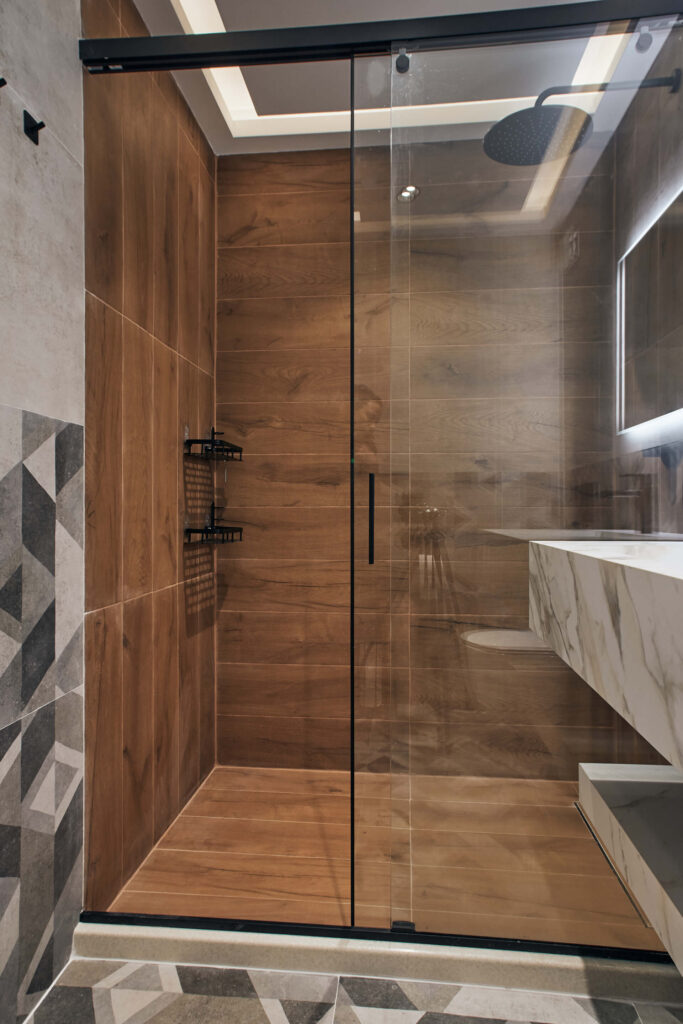Модерен душ от Интериорен дизайн Studio28a със стени с дървесен облик, стъклени врати и геометрични плочки на пода.