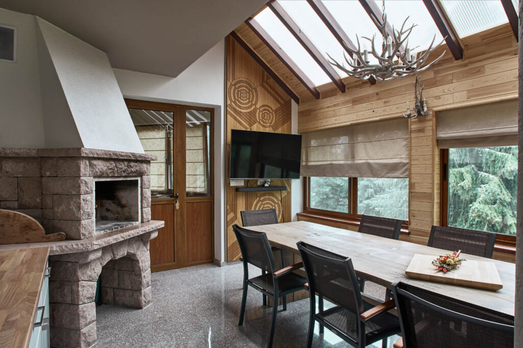 Модерна трапезария от Интериорен дизайн Studio28a с каменна камина, дървена маса, полилей от рог и гледка към дърветата.
