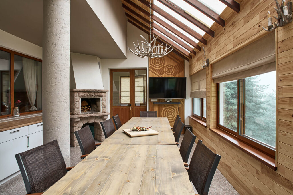 Трапезария от Интериорен дизайн Studio28a с дървена маса, полилей от рог, камина, телевизор и големи прозорци.