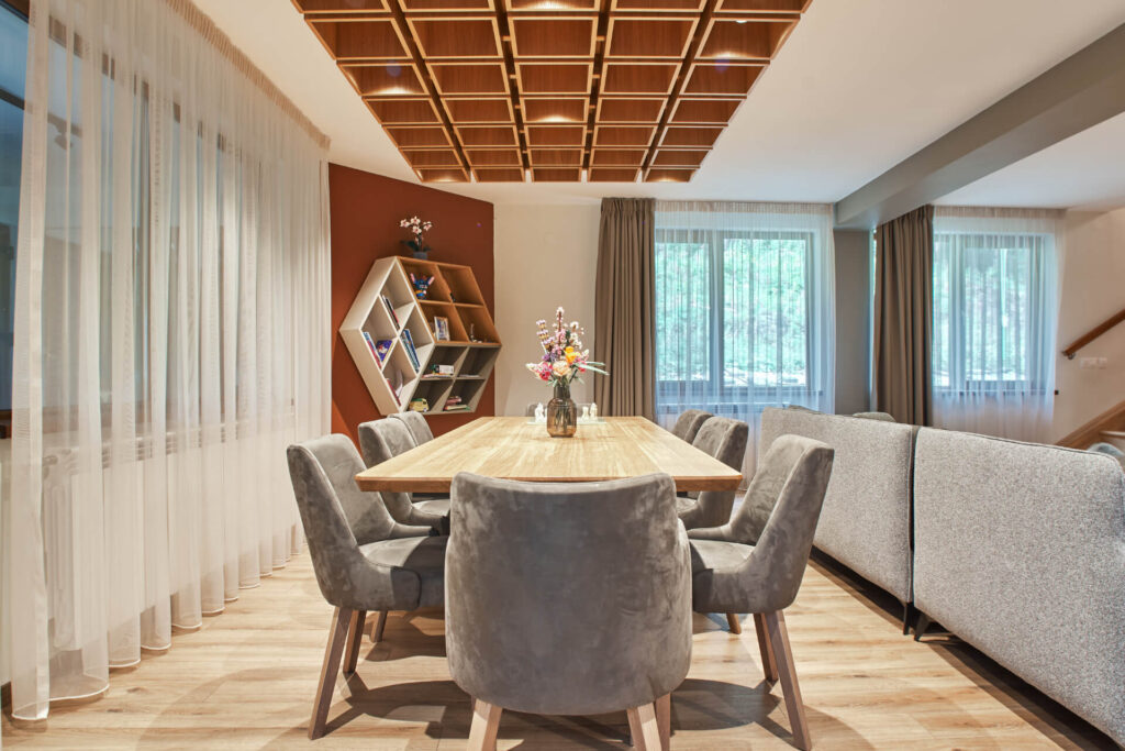 Модерна трапезария от Интериорен дизайн Studio28a с дървена маса, сиви столове, цветя и прозорци с прозрачни завеси.