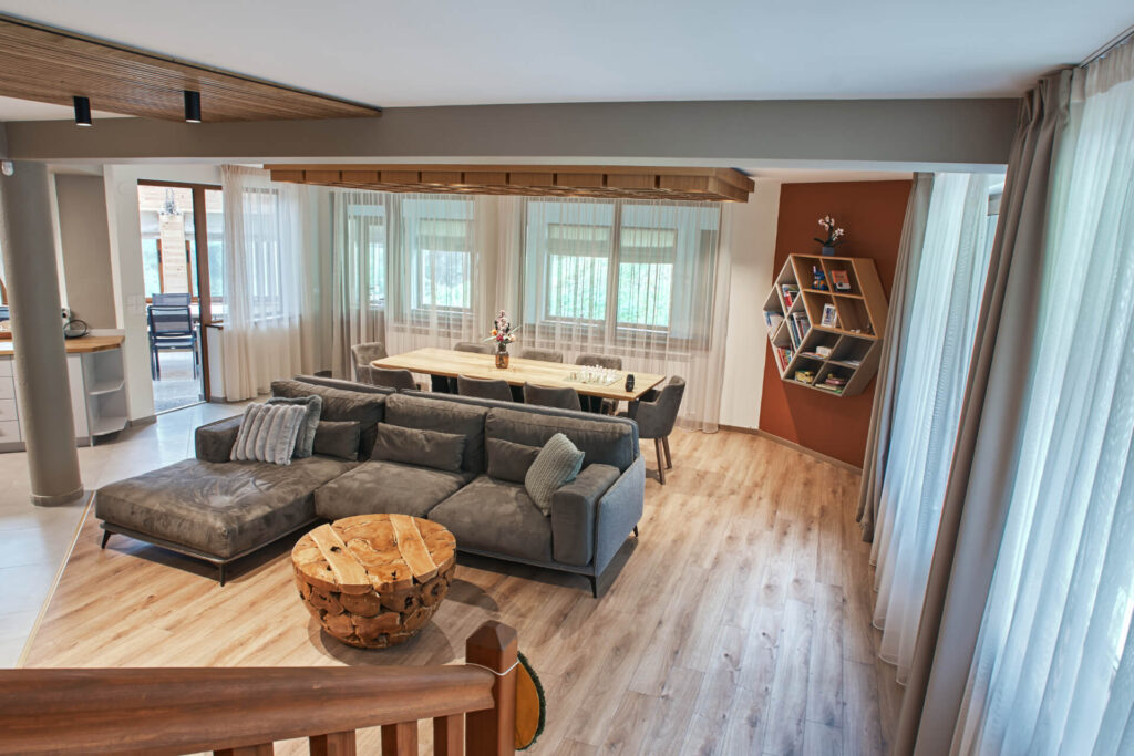 Модерна дневна от Интериорен дизайн Studio28a със сива секция, дървена маса, трапезария и големи прозорци.