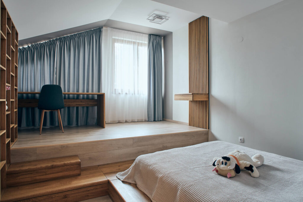 Модерна спалня от Интериорен дизайн Studio28a с легло с платформа, плюшена играчка крава, бюро и прозорец със синя завеса.