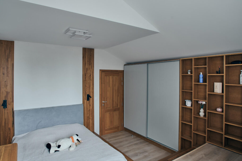 Модерна спалня от Интериорен дизайн Studio28a с дървена врата, плъзгащ се гардероб, отворени рафтове и легло с плюшена играчка.