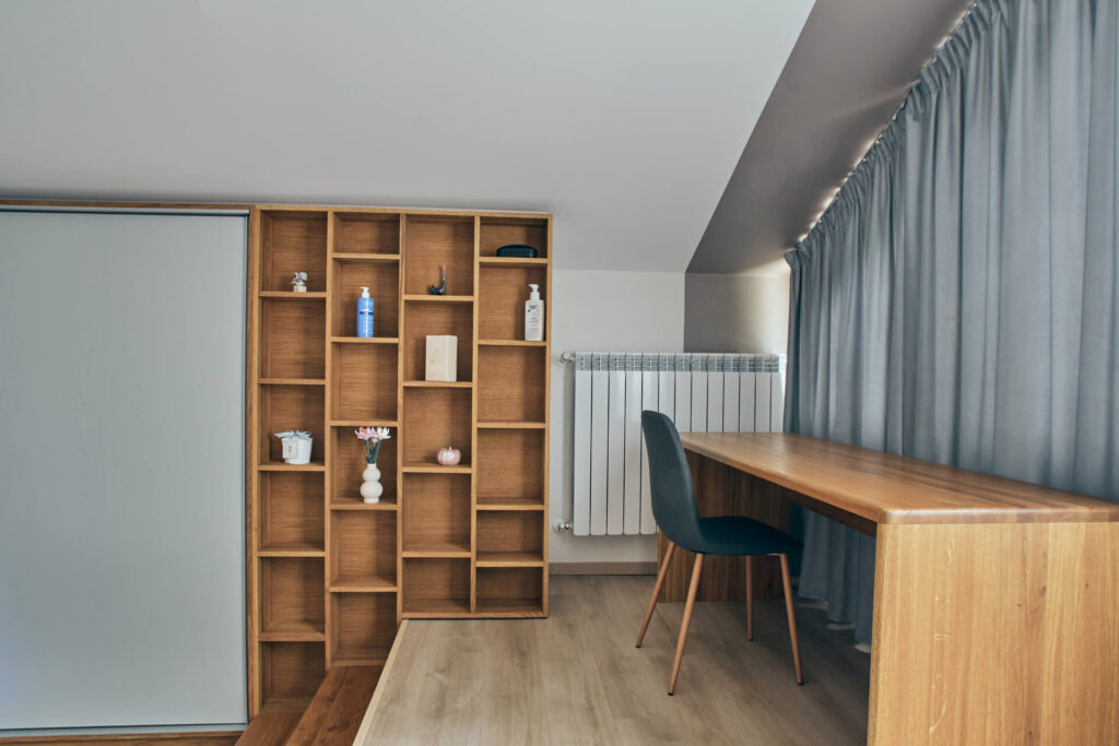 Минималистично работно пространство от Интериорен дизайн Studio28a с дървено бюро, тъмен стол, рафтове и сиви завеси.