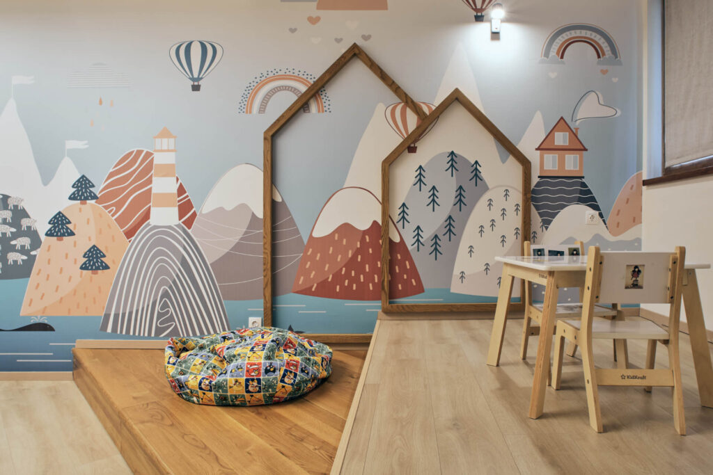 Детска стая за игра от Интериорен дизайн Studio28a със стенопис на планина, рамки за къщи, чувал за боб и детска маса.