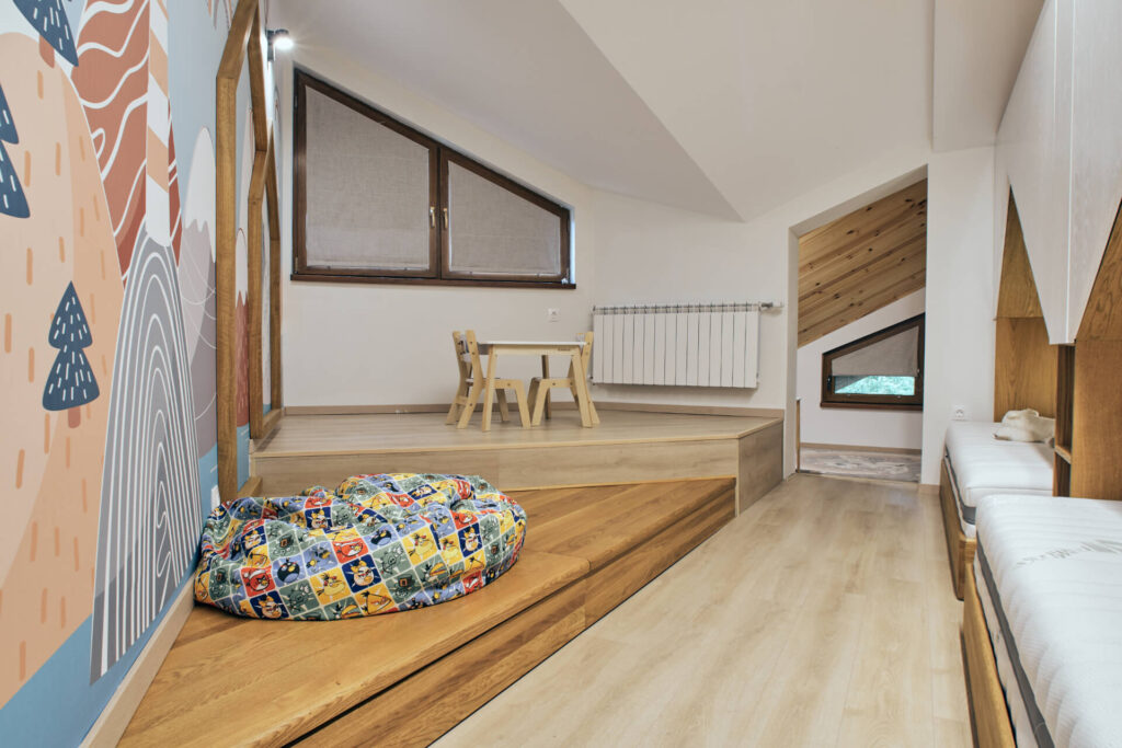 Детска стая за игра от Интериорен дизайн Studio28a с малка масичка, чувал за боб и геометричен декор на стената върху дървена подова настилка.