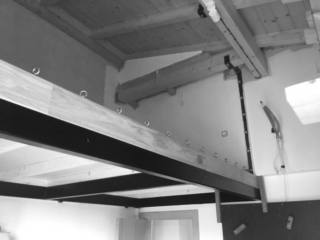 Дървена таванска платформа с открити греди и метални подпори от Интериорен дизайн Studio28a в незавършено помещение.